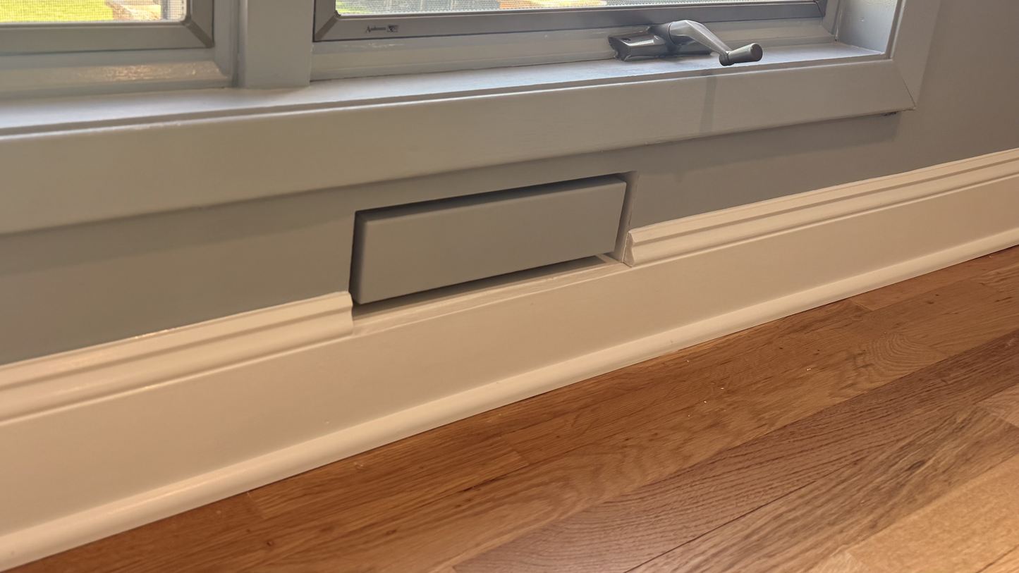 Seam flush wall vent installed below a window and painted to match the room's sage trim — demonstrating how the paintable powder-coat finish lets the vent integrate seamlessly with surrounding millwork